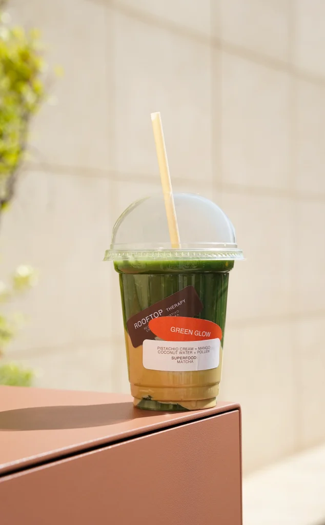 Vaso de Green Glow con la etiqueta de Rooftop Therapy sobre el muro del rooftop Furtivo — Barcelona
