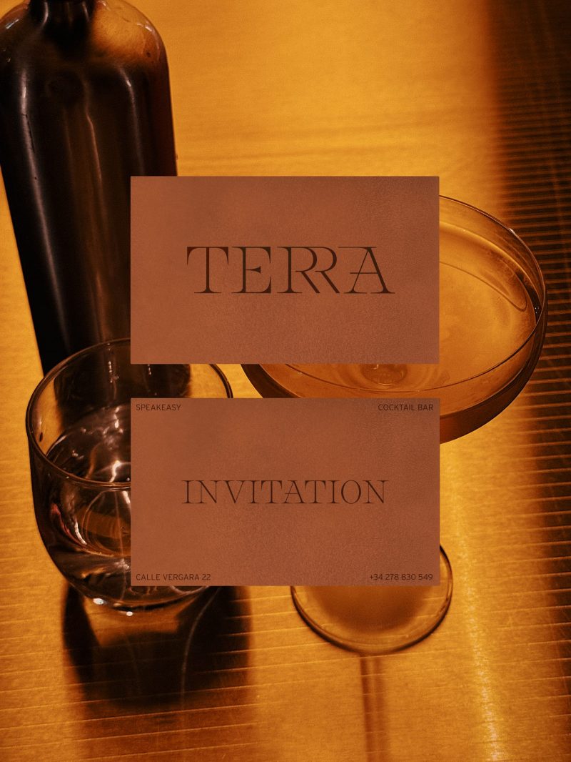 Tarjeta de invitación de Terra en tono terracota junto a una copa de cóctel